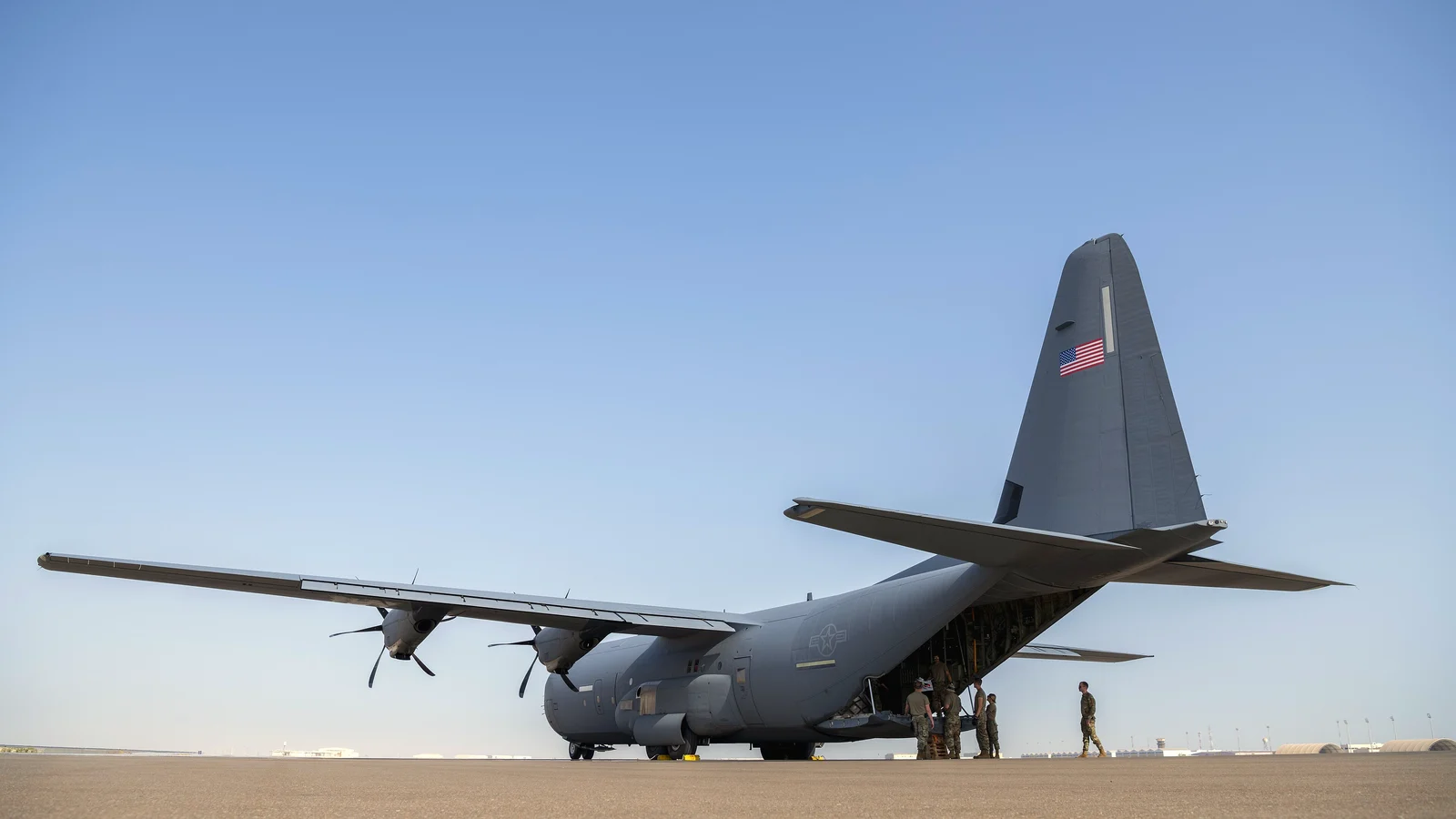 Ground crew loading cargo onto a military transport aircraft with its rear ramp down