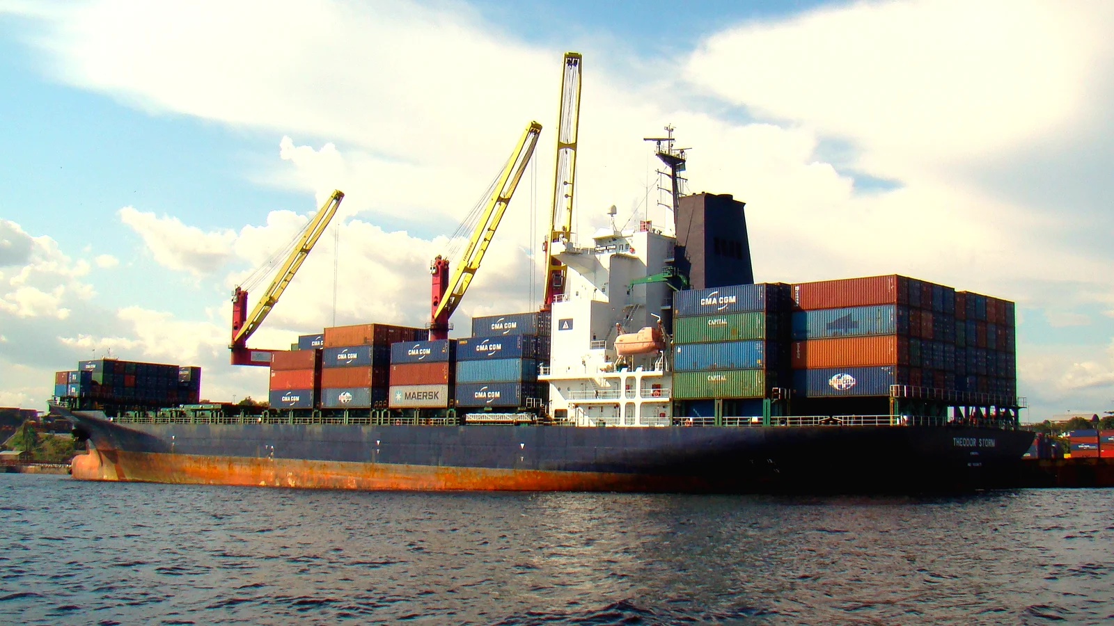 Container ship loading at a quay with ship cranes on a sunny day