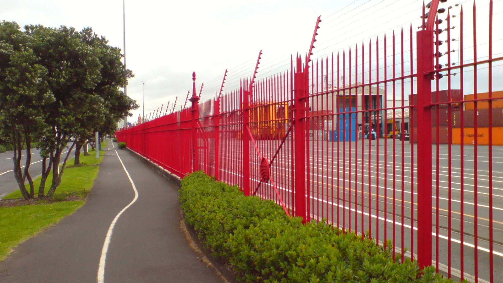 Tall security fence around a port container terminal beside a public path