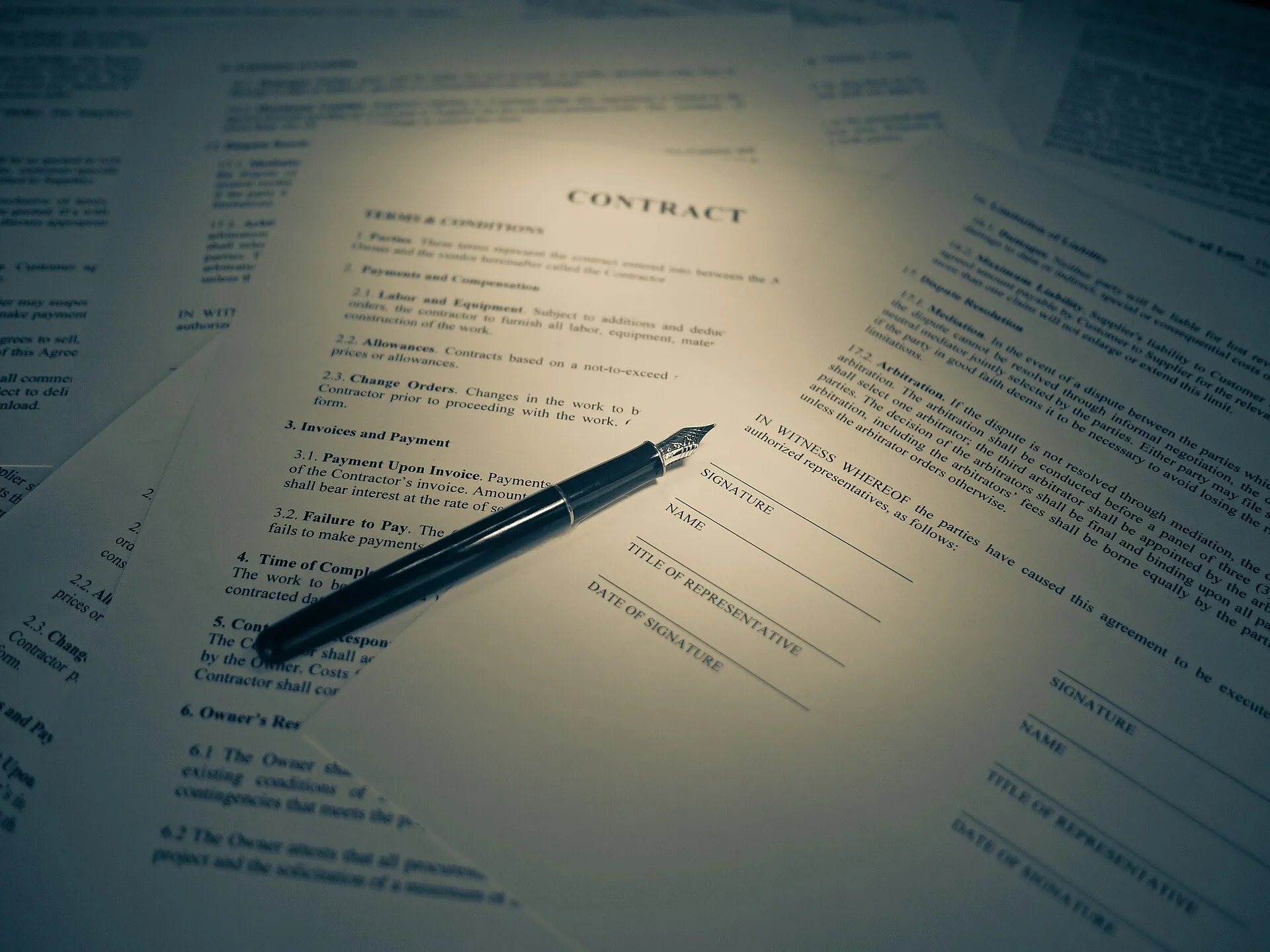 Printed contract with signature lines and a fountain pen lying on a desk among other documents