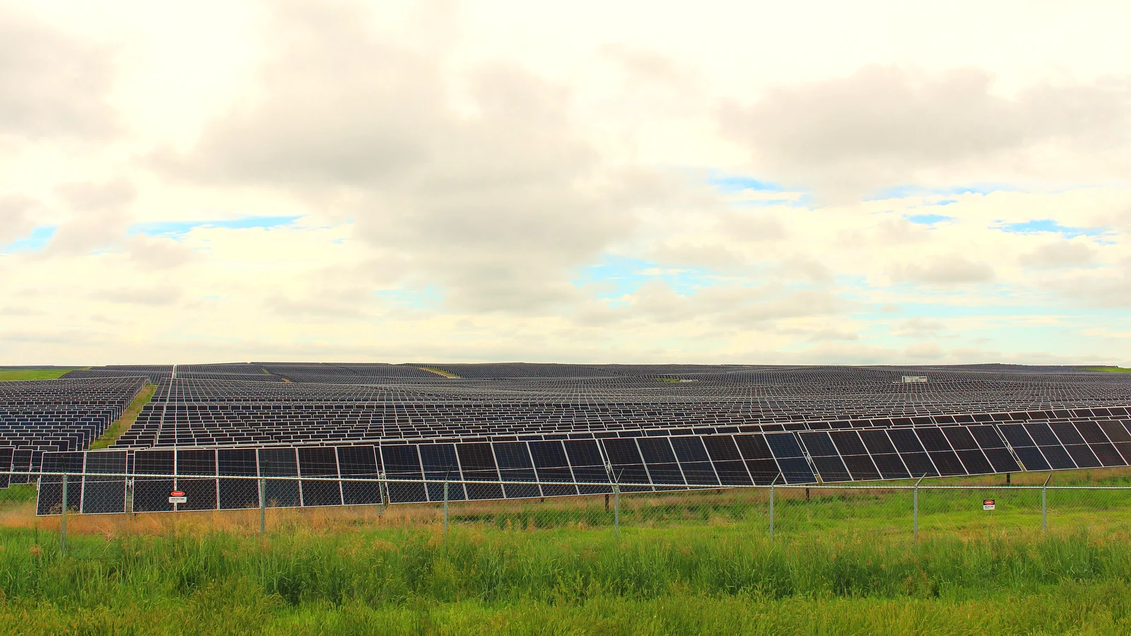 Rows of photovoltaic panels at a utility-scale solar farm under a cloudy sky