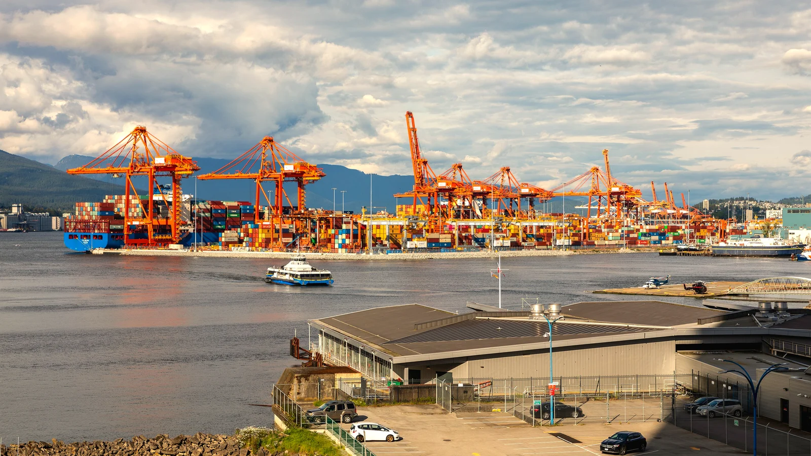 Orange gantry cranes and container stacks at Centerm terminal in Vancouver with mountains behind