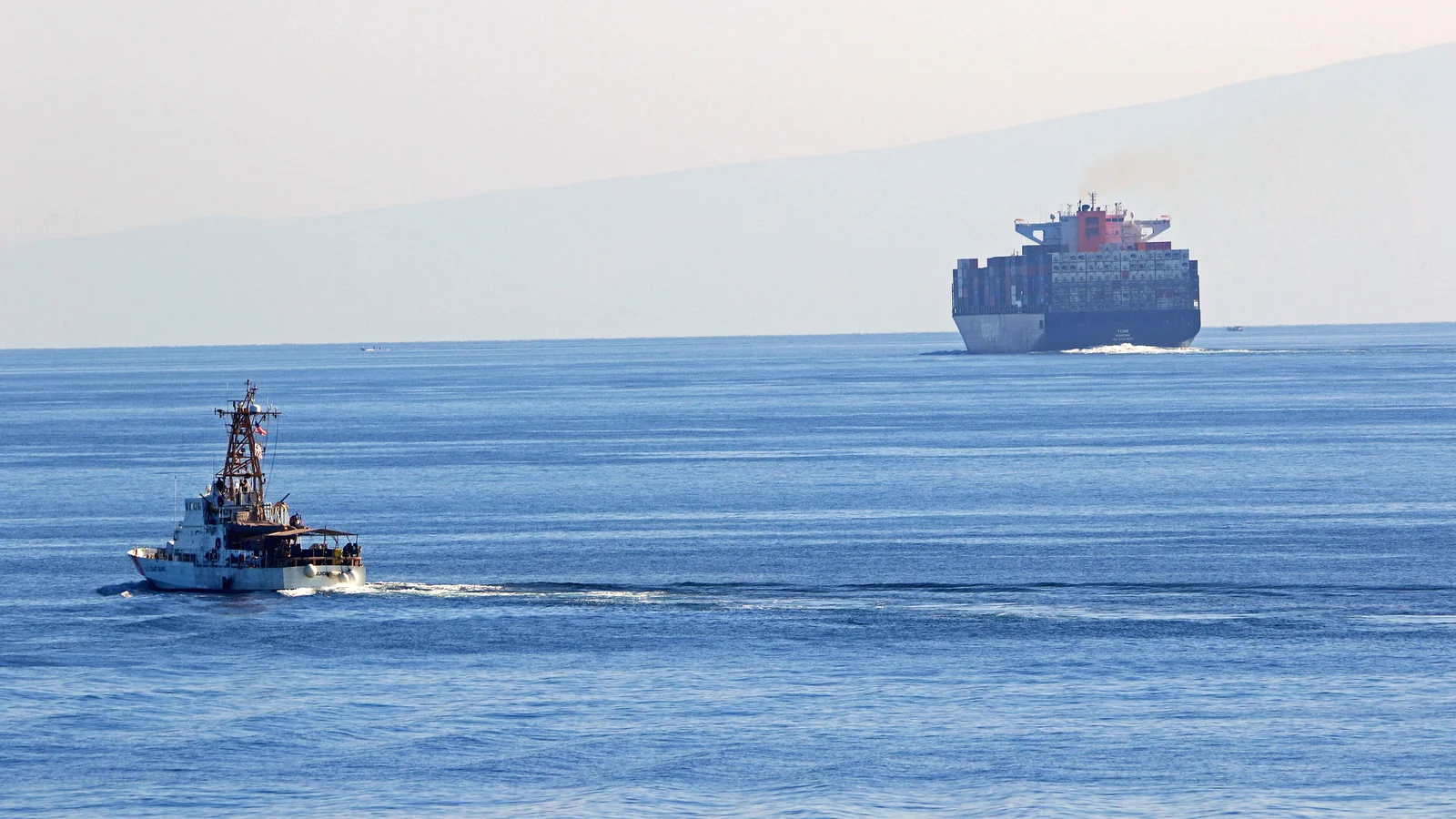 Container ship and a patrol cutter crossing the Strait of Hormuz in daylight