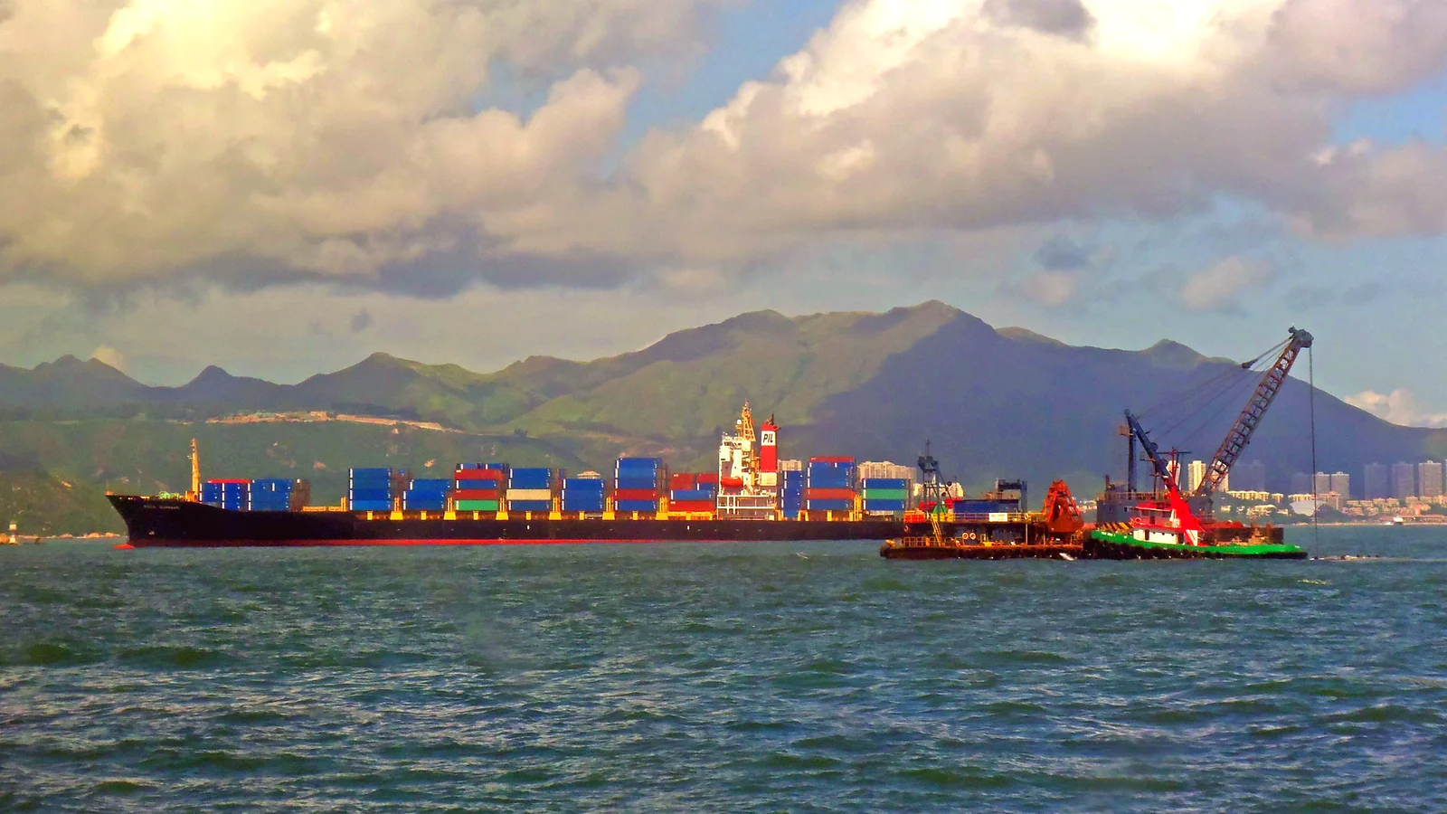 Container ship and small boats in Hong Kong Harbor under a cloudy sky