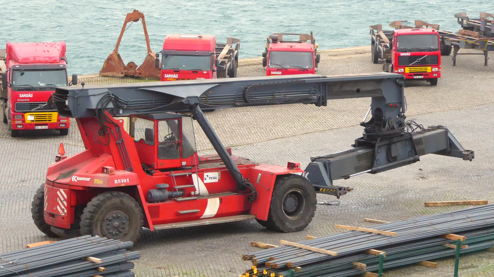 Red reach stacker container handler parked on a quay with trucks behind