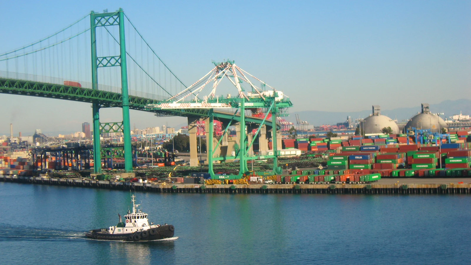 Vincent Thomas Bridge over the harbor with container terminal cranes and a tug